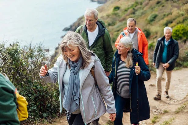 Gruppo di anziani che camminano insieme su un sentiero costiero con vista sul mare