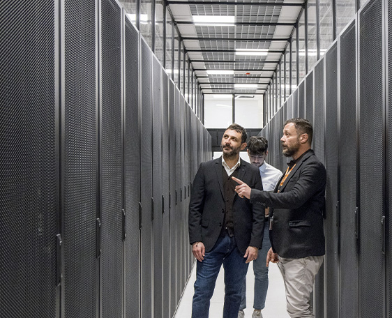 Tre uomini in abiti formali camminano in corridoio con server informatici