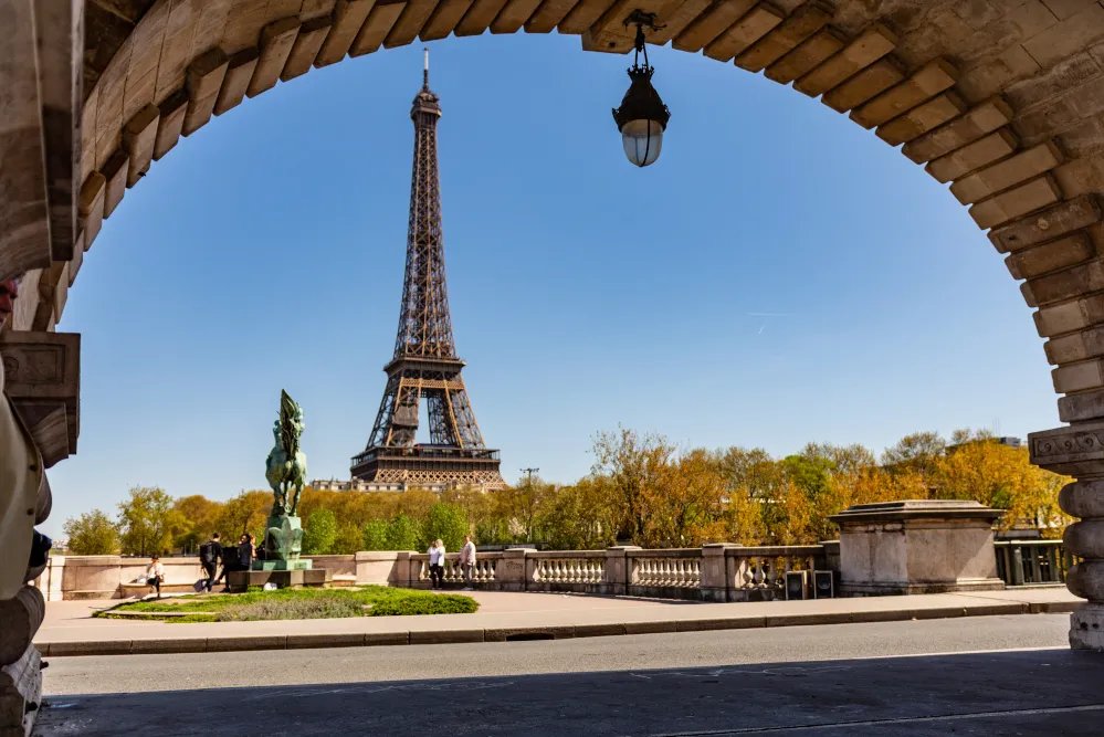 Veduta della Torre Eiffel attraverso un arco in pietra con alberi autunnali sullo sfondo a Parigi
