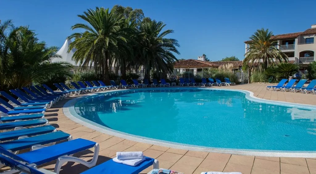 Piscine rectangulaire turquoise avec chaises longues bleues et palmiers en arrière-plan.